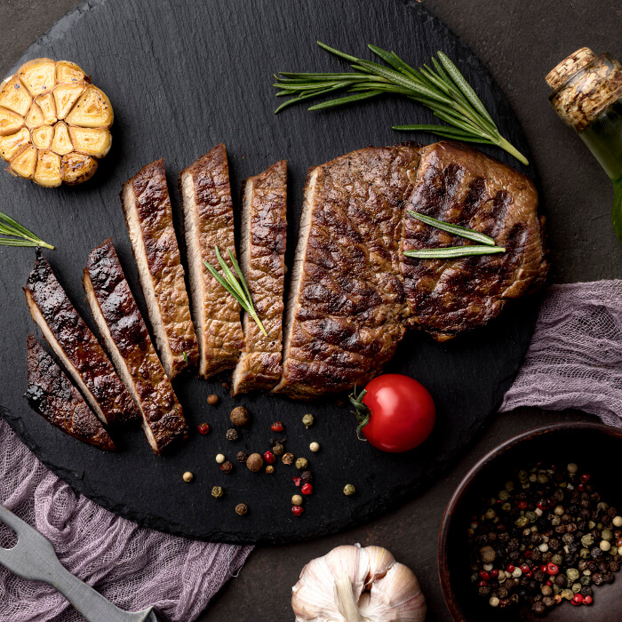 Steak on a black cutting board with whole peppers
