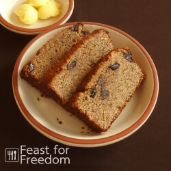 Slices of banana bread with raisins on a plate, with a small dish of butter next to it