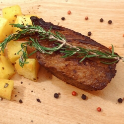 Cut of marinated beef steak with rosemary and cubed potatoes on a cutting board