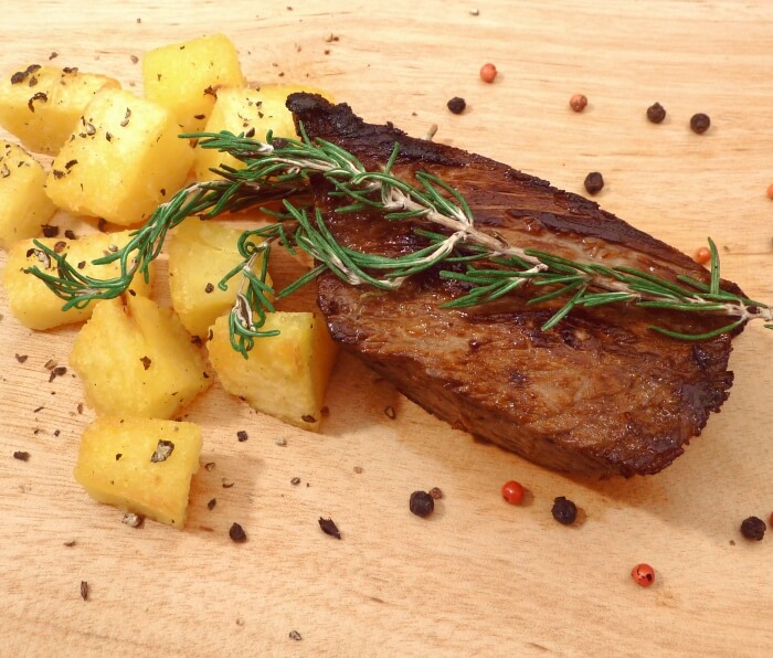 Cut of marinated beef steak with rosemary and cubed potatoes on a cutting board