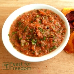 Freshly made salsa in a bowl next to a variety of different types of potato chips
