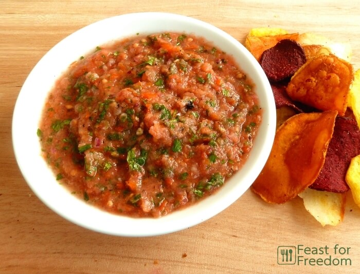 Freshly made salsa in a bowl next to a variety of different types of potato chips