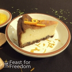 New York style baked cheesecake on a plate, next to a small bowl of Mango Sauce, sprinkled with orange and lime zest