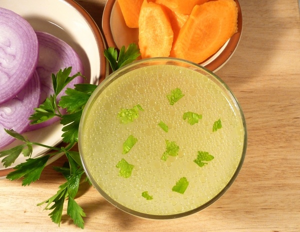 Chicken stock in a clear glass bowl with carrots and onions