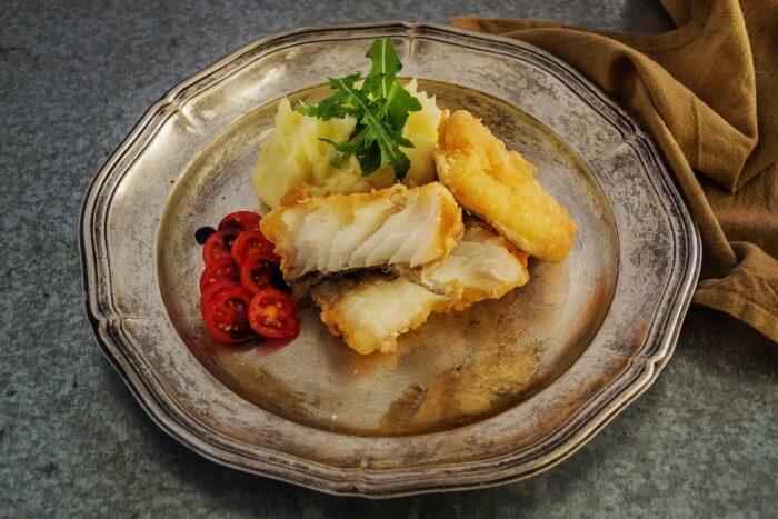 Deep fried fish on an antique silver plate with sliced grape tomaotes