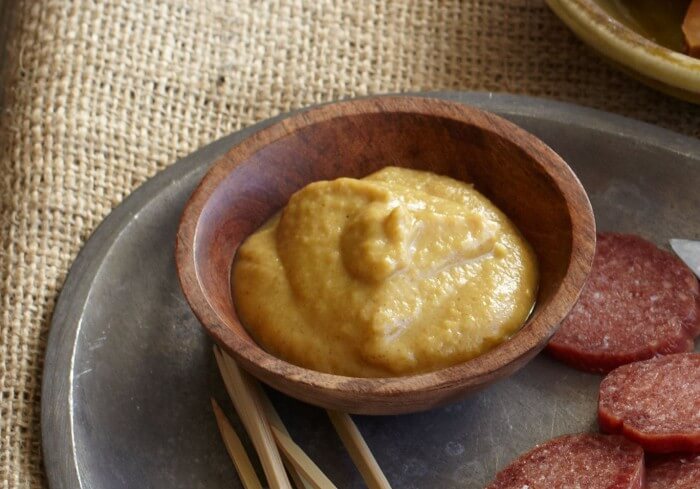 Dijon mustard in a small wooden bowl on a platter with sausage medallions