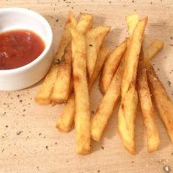 Homemade French Fries on a wooden board next to a small dish of ketchup