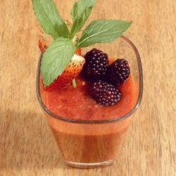 Strawberry, blackberry and peach fruit smoothie in a tall glass with a fresh strawberry and blackberry garnish