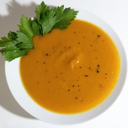 Ginger squash soup in a bowl with a sprig of parsley and fresh ground pepper.
