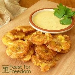 Fried Patacones on a wooden platter with a dish of garlic and lime mayo dip