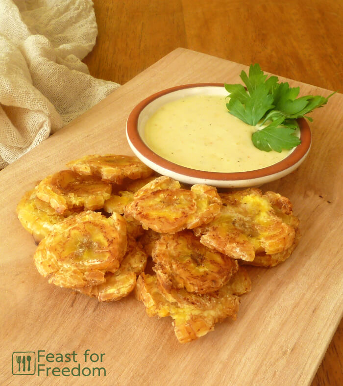 Fried Patacones on a wooden platter with a dish of garlic and lime mayo dip