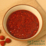A bowl of fresh raspberry sauce with some raspberries next to it